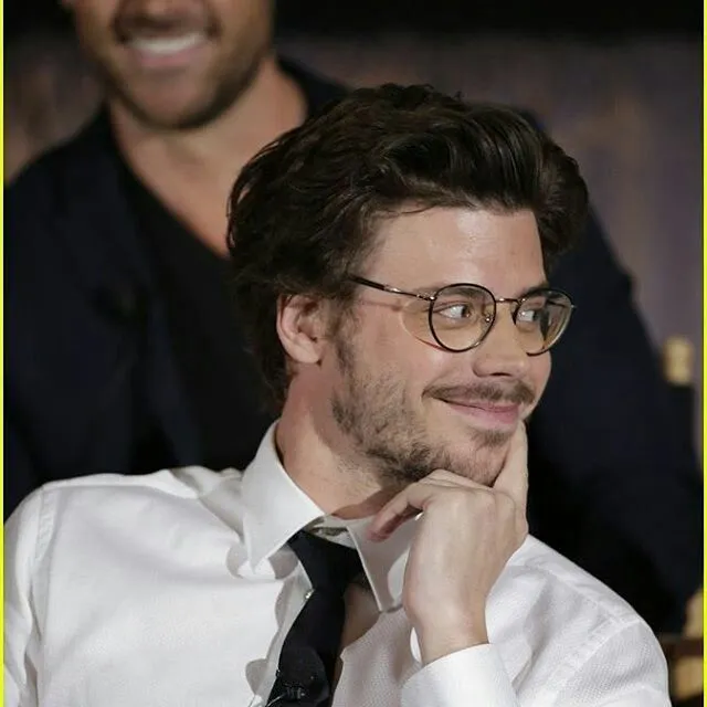 a man wearing glasses and a white shirt is smiling at the camera with his hand on his chin
