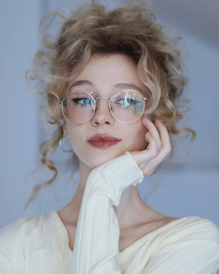 a woman wearing glasses with her hand on her chin and looking off to the side