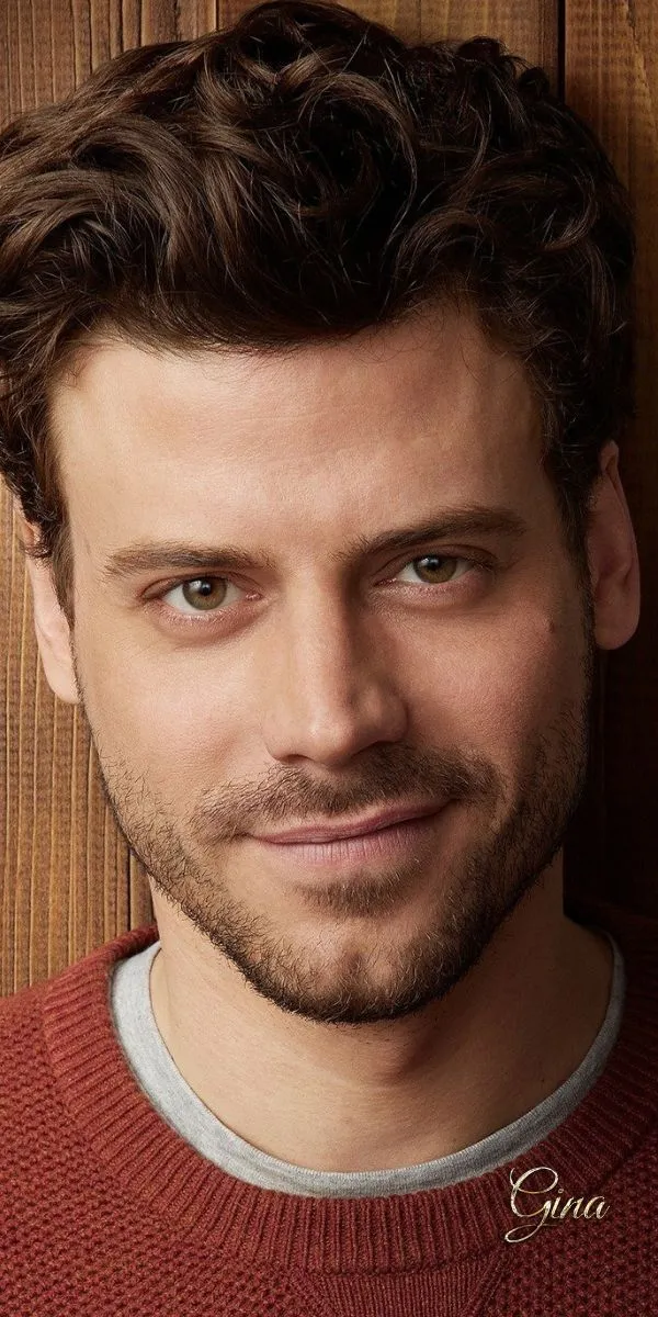 a close up of a person wearing a sweater and smiling at the camera with wood background