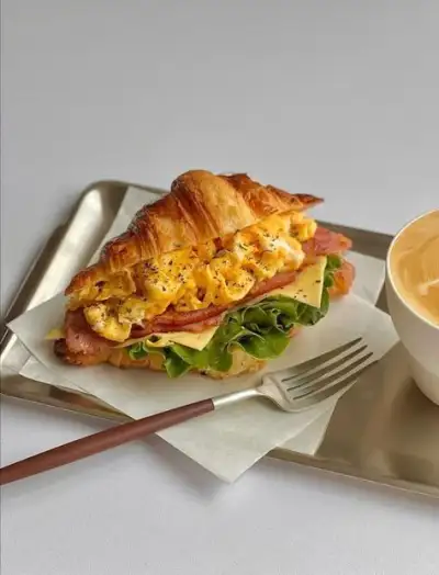 a breakfast sandwich on a tray next to a cup of cappuccino coffee