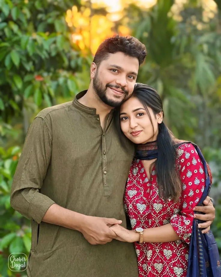 two people standing next to each other in front of trees