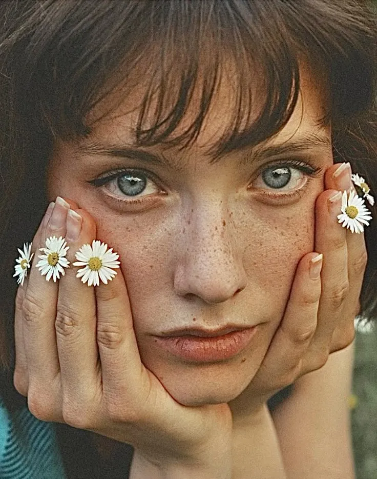 a woman with freckles on her hands and daisies in front of her face