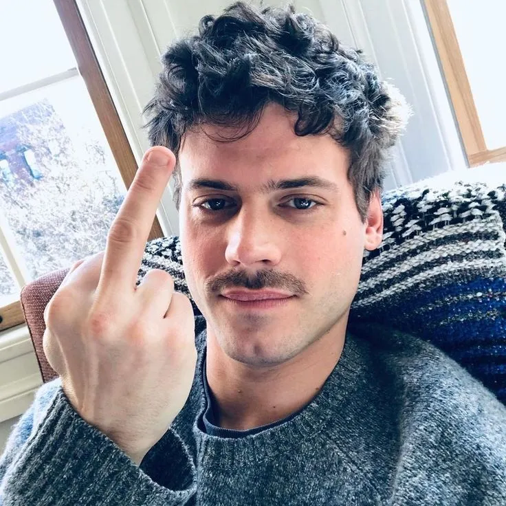 a man making the middle finger sign with his hand while sitting in front of a window