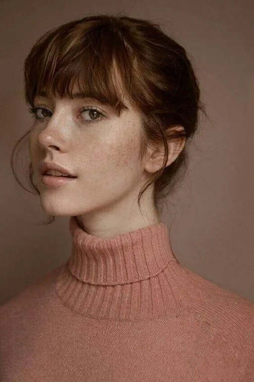 a woman with freckled hair wearing a pink turtle neck sweater looking at the camera