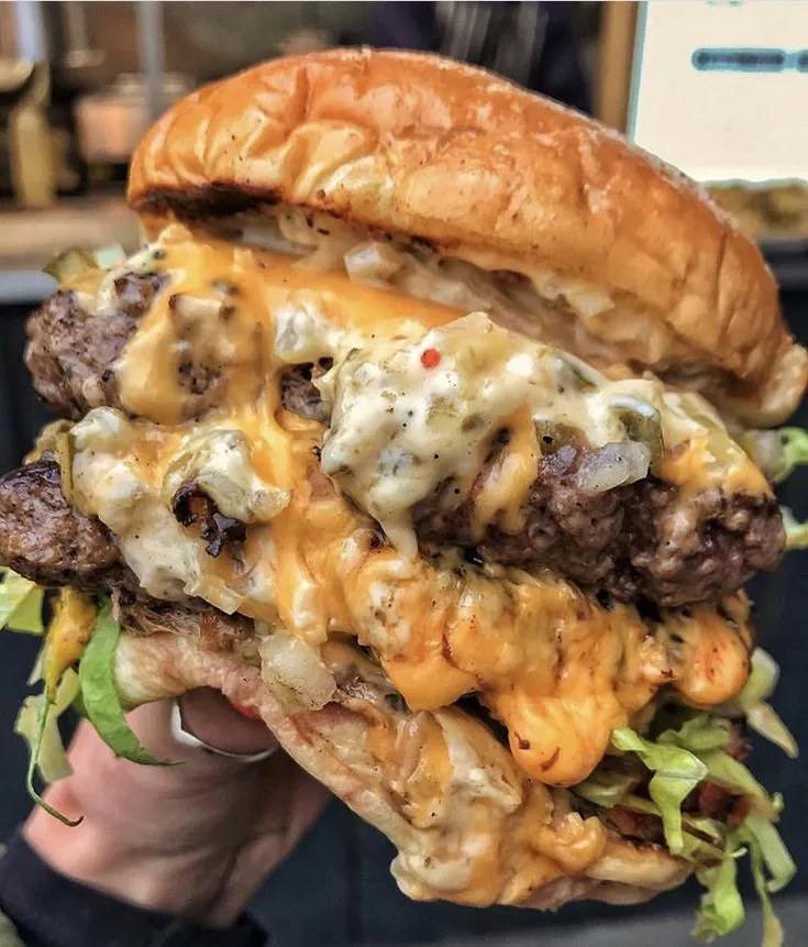 a person holding up a cheeseburger with meat and lettuce on it