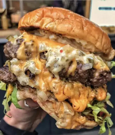 a person holding up a cheeseburger with meat and lettuce on it