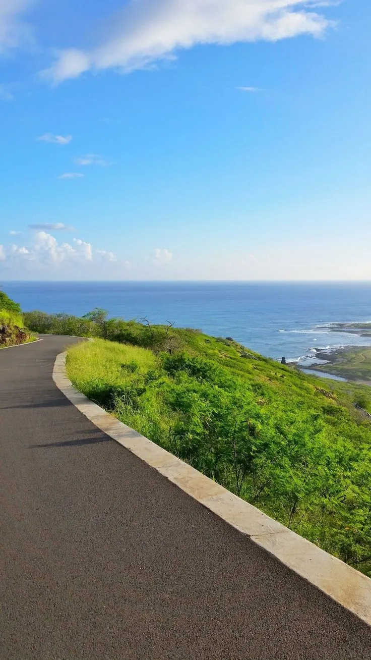 an empty road next to the ocean on a sunny day