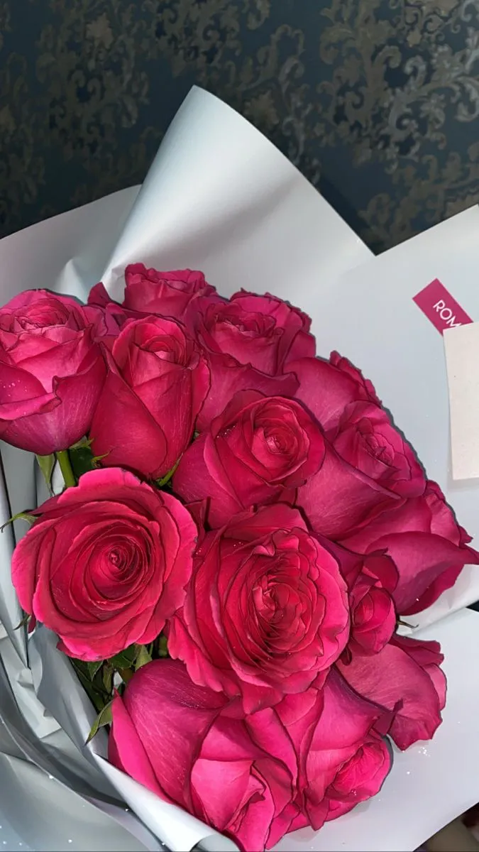 a bouquet of pink roses sitting on top of a white tablecloth with a note attached to it