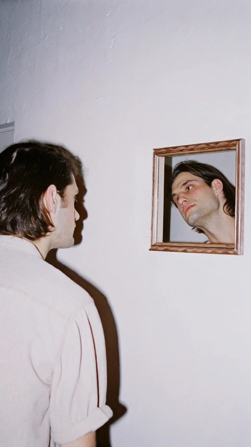 Man with medium-length dark hair staring at a mirror, reflection...