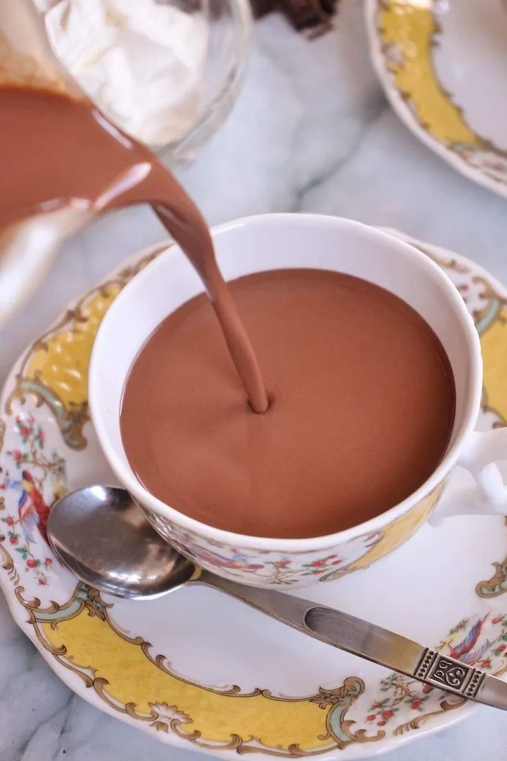 a cup of hot chocolate is being poured into a saucer with a spoon on the side