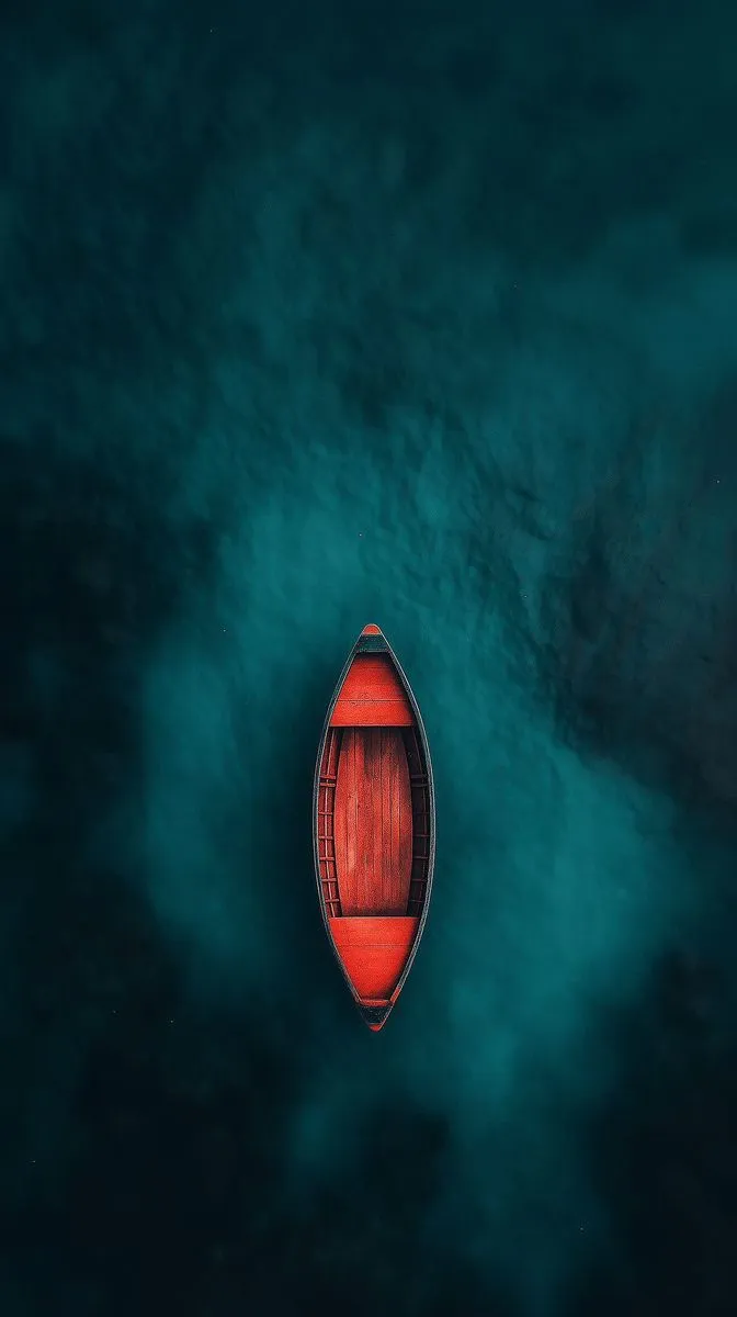 an aerial view of a red boat in the middle of blue water with clouds around it
