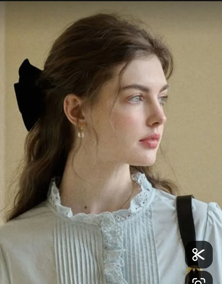 a woman wearing a white blouse with a black bow in her hair is looking off to the side