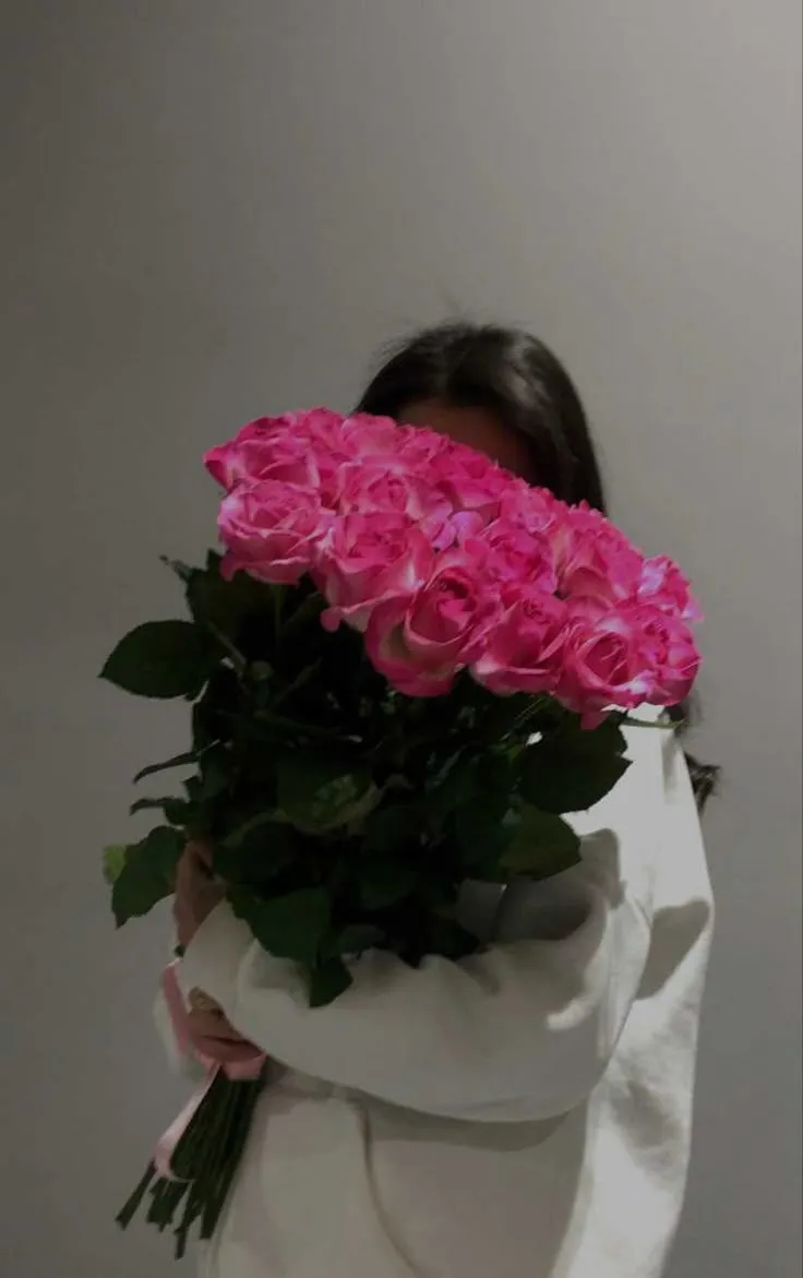 a woman holding a bouquet of pink roses in her arms and covering her face with a white blanket