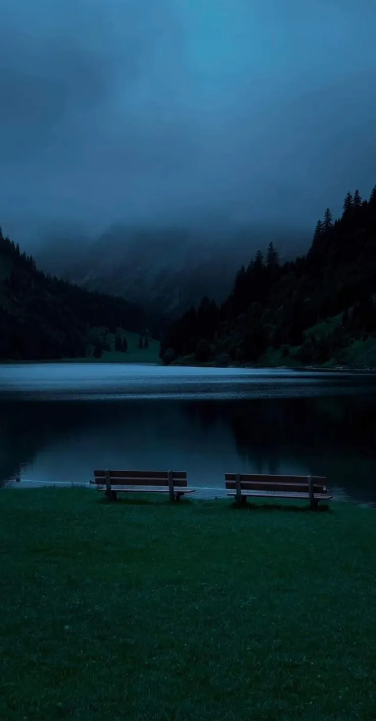 two wooden benches sitting in front of a body of water under a dark cloudy sky