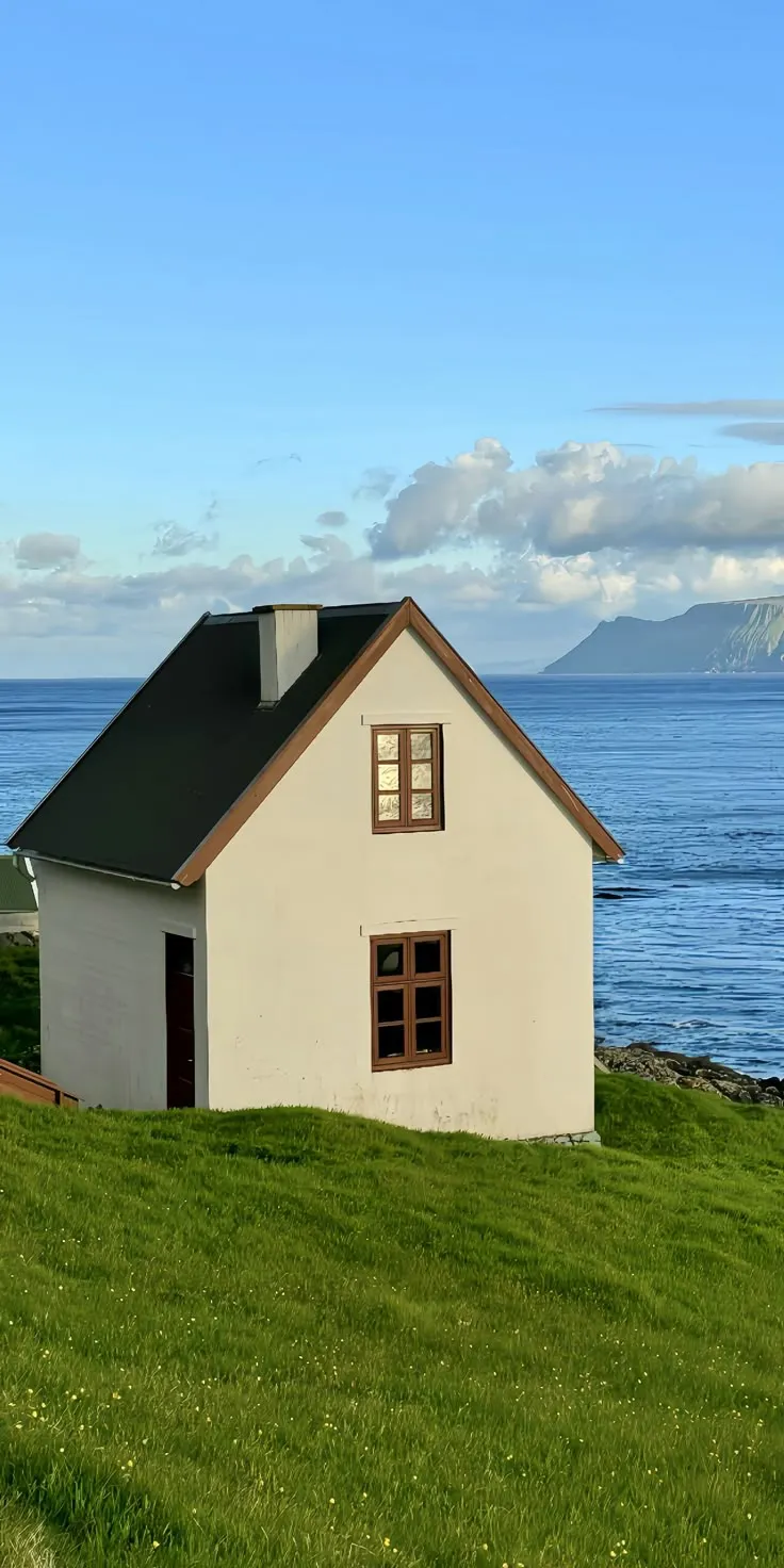 a small white house sitting on top of a lush green field next to the ocean