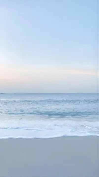 an empty beach with waves coming in to shore and the sky is blue, white and pink