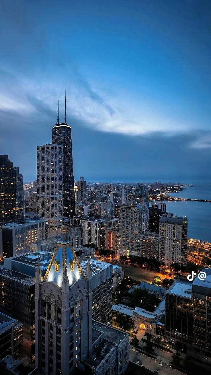 the city skyline is lit up at night with skyscrapers in the foreground and water below