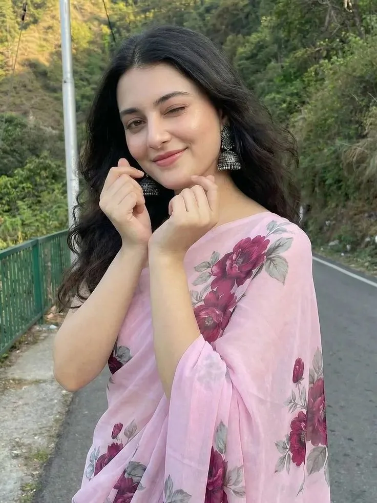 a woman in a pink sari standing on the side of a road with her hand under her ear