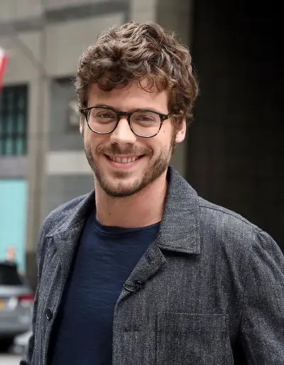 a man with glasses is standing in front of a building and smiling at the camera