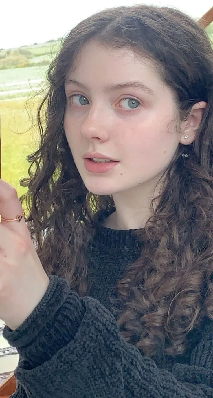 a woman with curly hair and blue eyes is holding an apple in her hand while looking at the camera