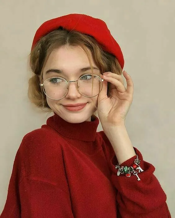 a young woman wearing glasses and a red hat poses for the camera with her hand on her head