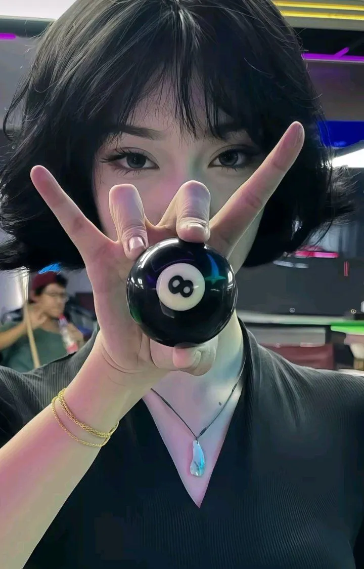 a woman holding up her hand with a pool ball in front of her face and the number eight on it