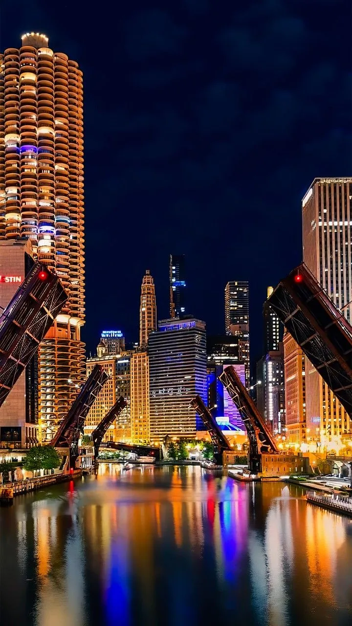 the city is lit up at night with lights reflecting in the water and skyscrapers