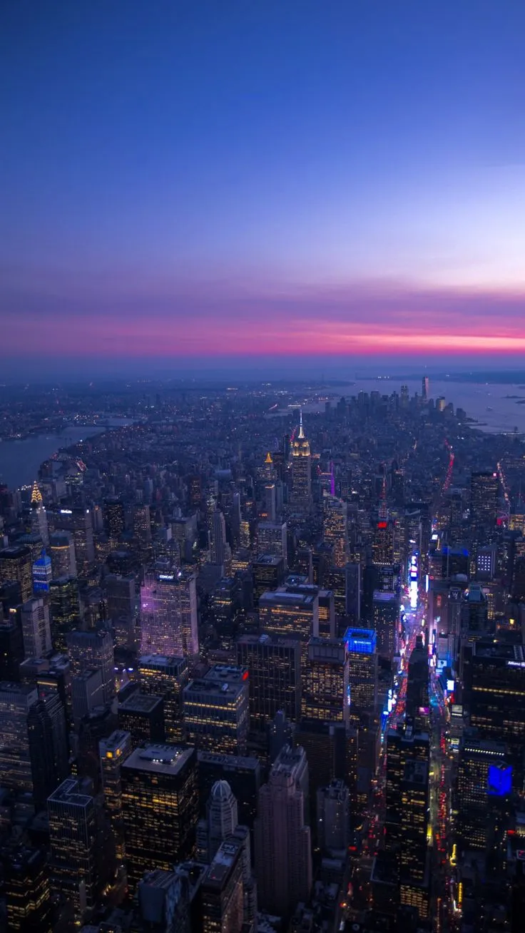 an aerial view of the city at night with lights and skyscrapers in the foreground