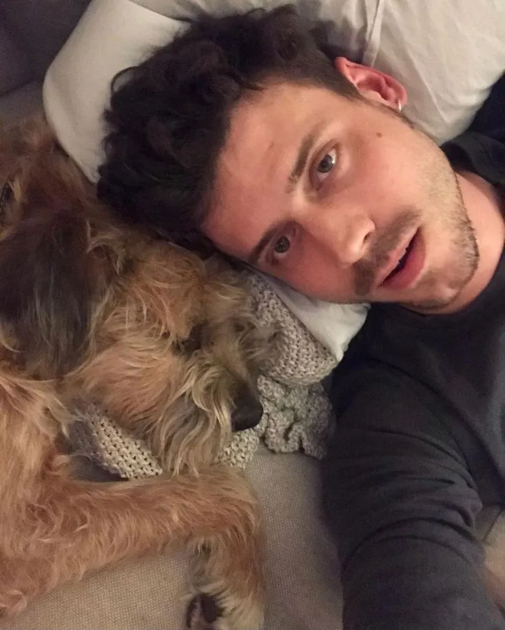 a man laying on top of a couch next to a brown dog and white pillows