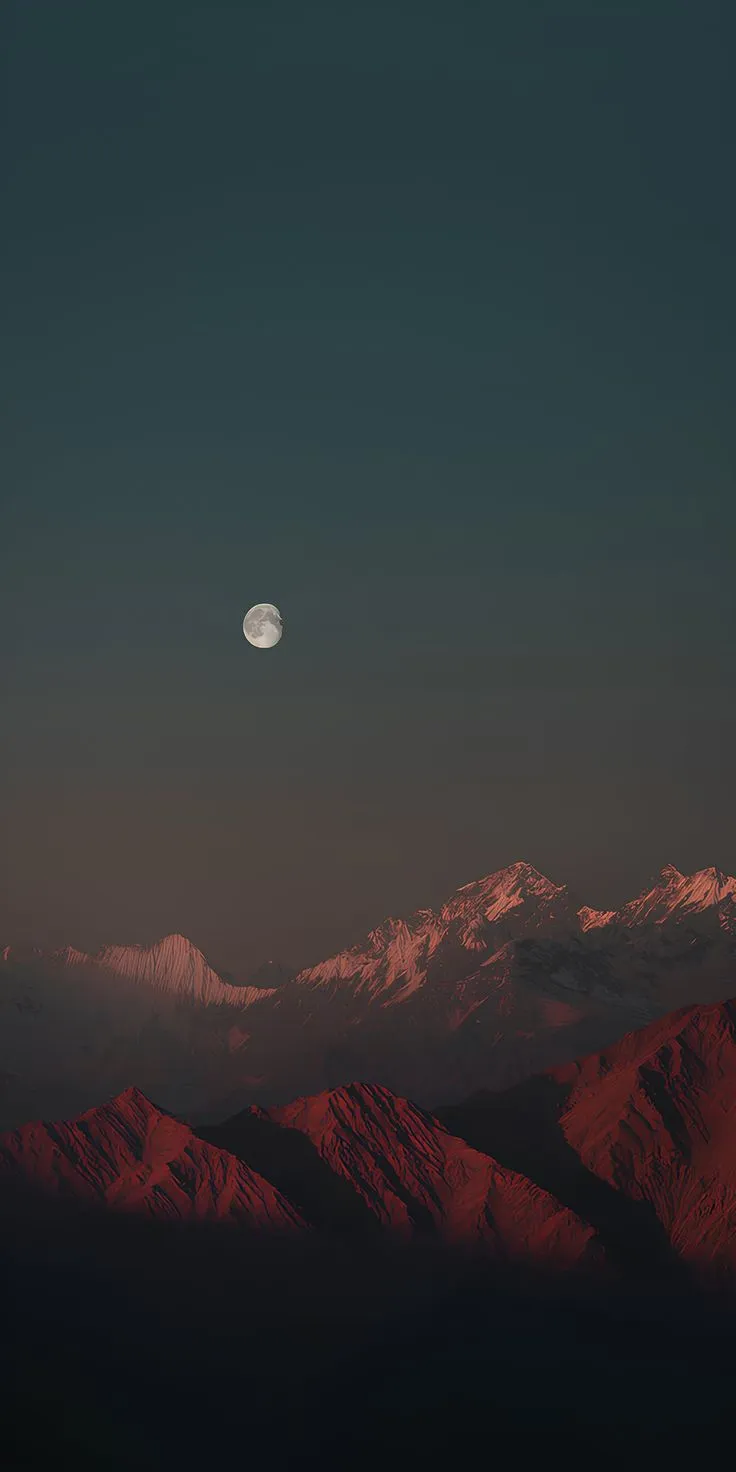 the moon is setting over mountains with snow on them