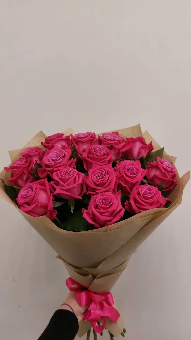 a bouquet of pink roses is held by a person's hand against a white wall