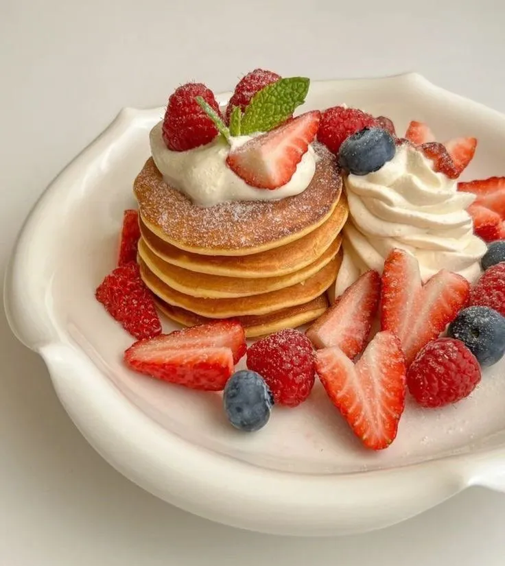pancakes with whipped cream, strawberries and blueberries on a white plate