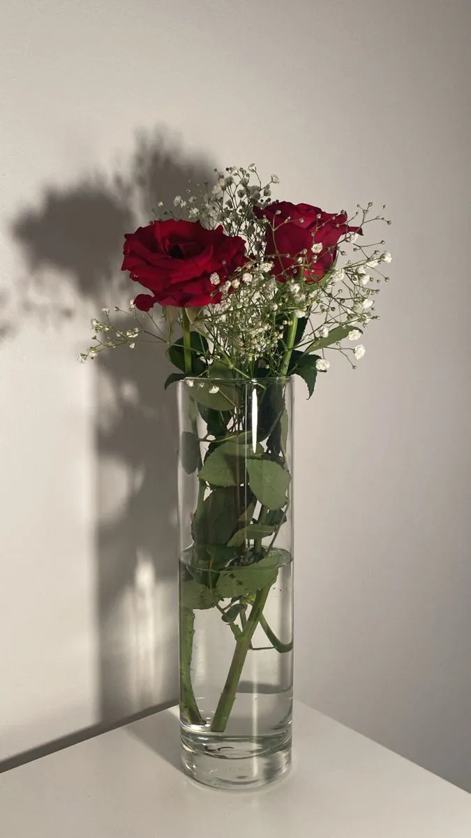 a vase filled with water and flowers on top of a white table next to a wall