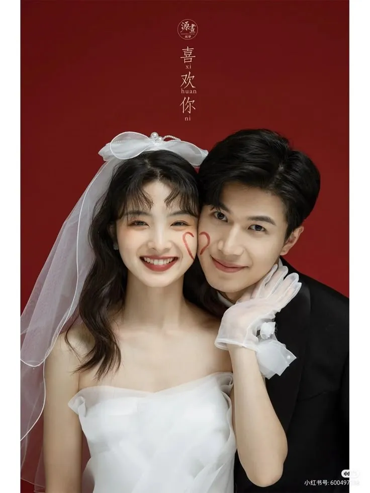 two people standing next to each other in front of a red wall with chinese characters on it