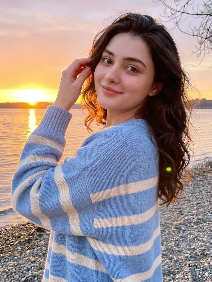 a woman standing on top of a rocky beach next to the ocean with her hand in her hair