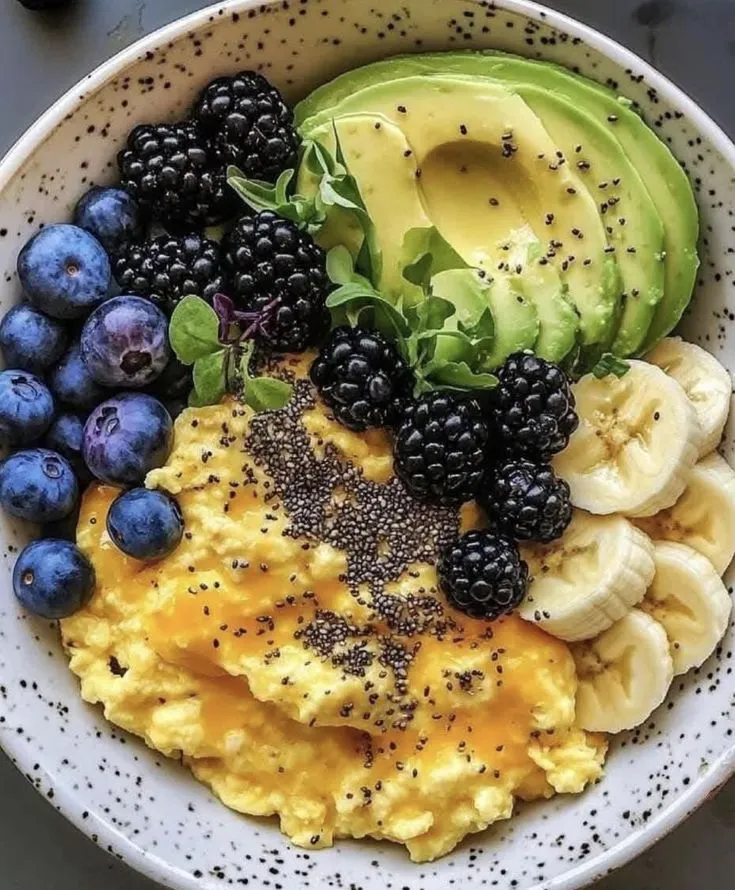 a bowl filled with eggs, fruit and avocado on top of a table