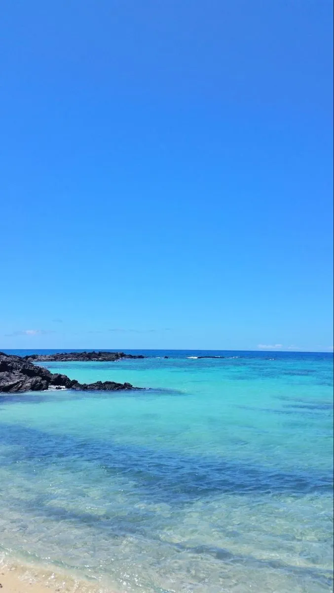 an empty beach with clear blue water on a sunny day
