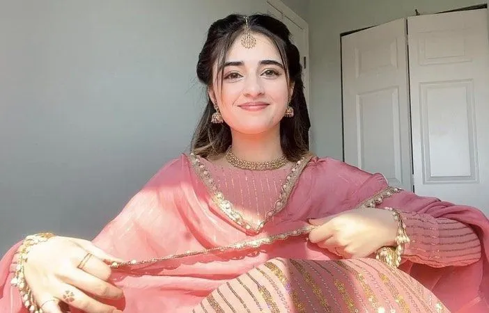 a woman in a pink dress is holding a gold necklace