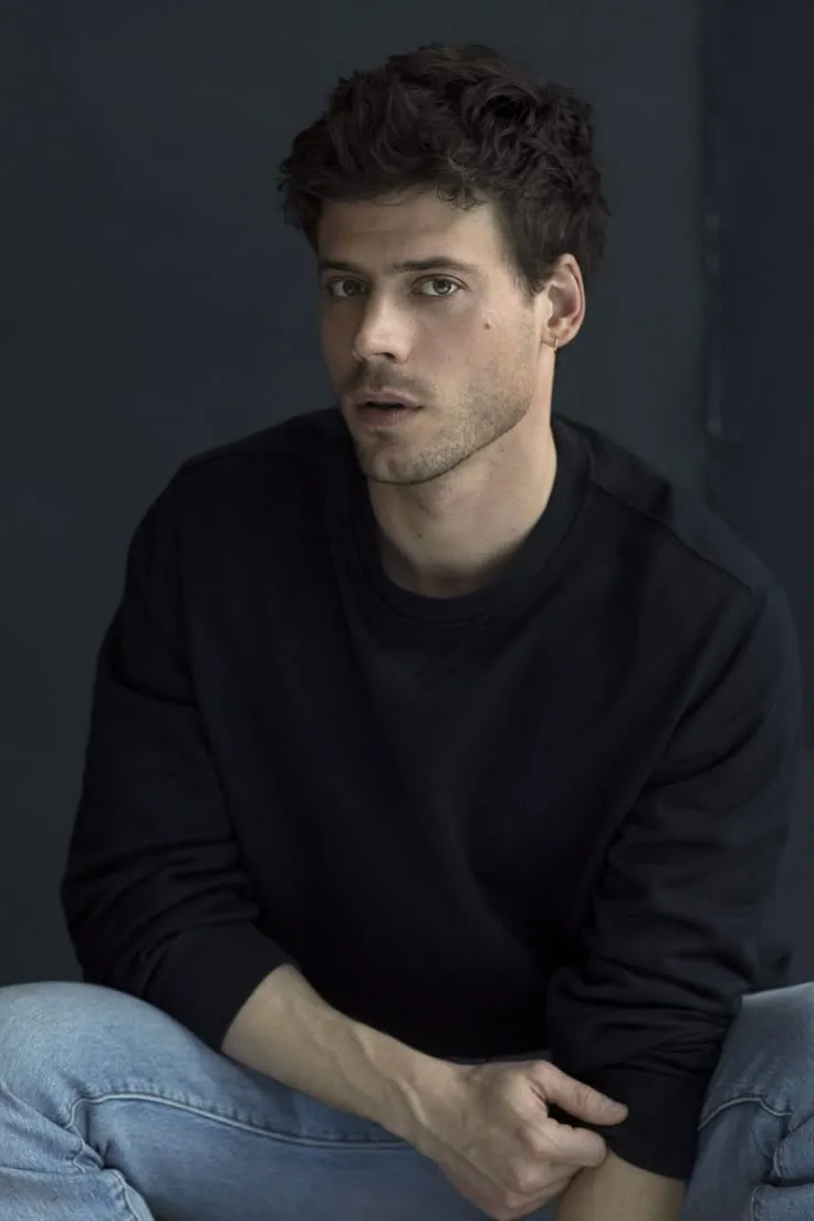 a man sitting on the ground with his hands in his pockets and looking at the camera