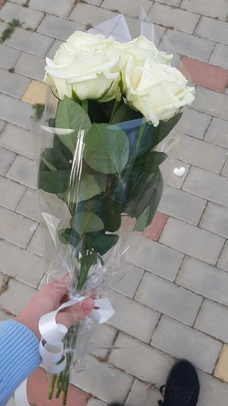 a person holding a bouquet of white roses on a brick walk way in the city