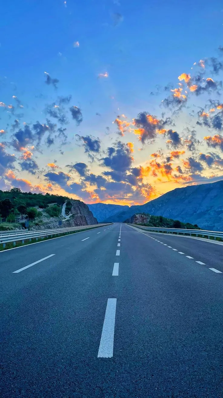 the sun is setting on an empty road with mountains in the background and clouds in the sky
