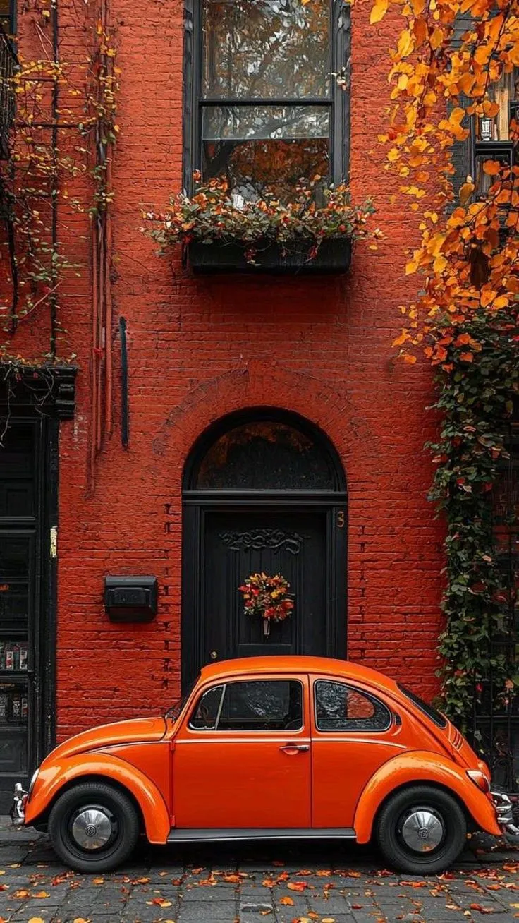 an orange car parked in front of a red brick building with autumn leaves on the ground