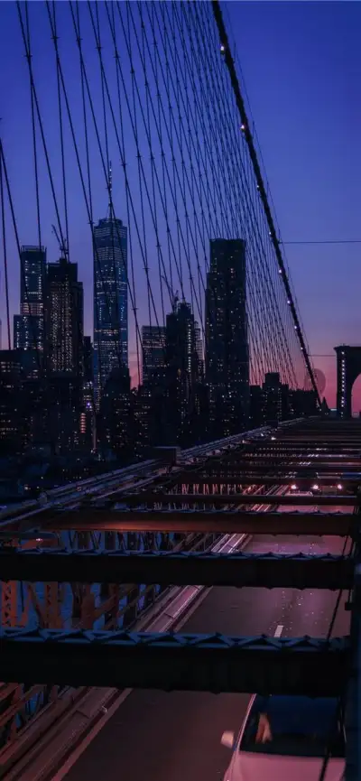 the city skyline is lit up at night as people walk across the bridge over the water