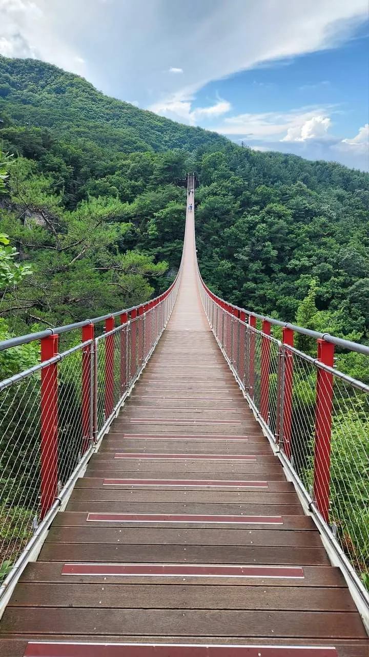 a long bridge with red railings going over a mountain