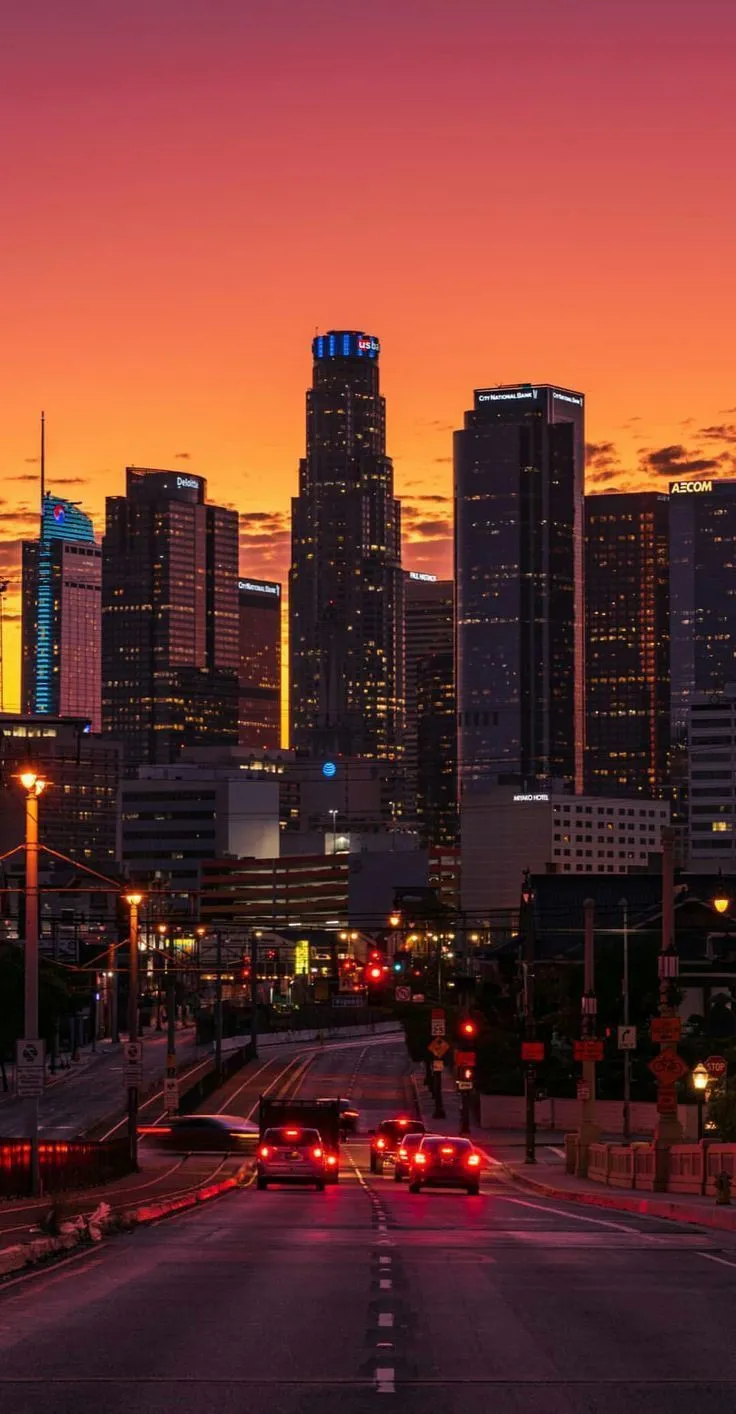 the city skyline is lit up at night with cars driving down the street in front of it