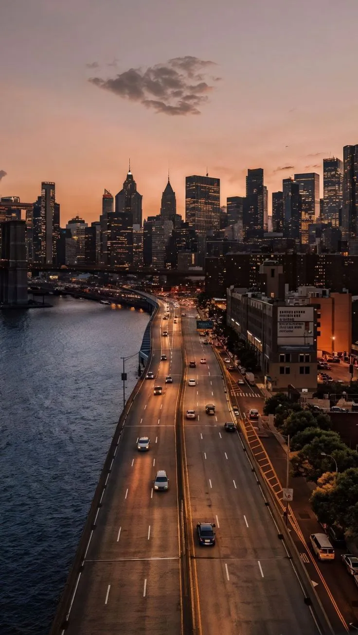 the city skyline is lit up at night as cars drive down an empty highway in front of tall buildings
