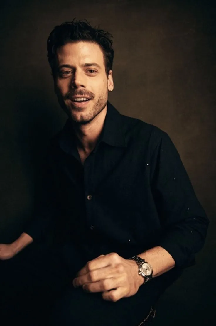 a man with a watch on his left hand is posing for a photo in front of a dark background