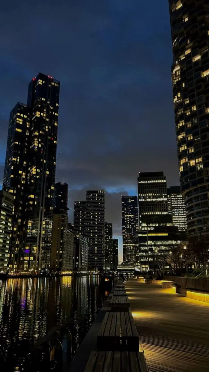 the city skyline is lit up at night with lights reflecting in the water and skyscrapers