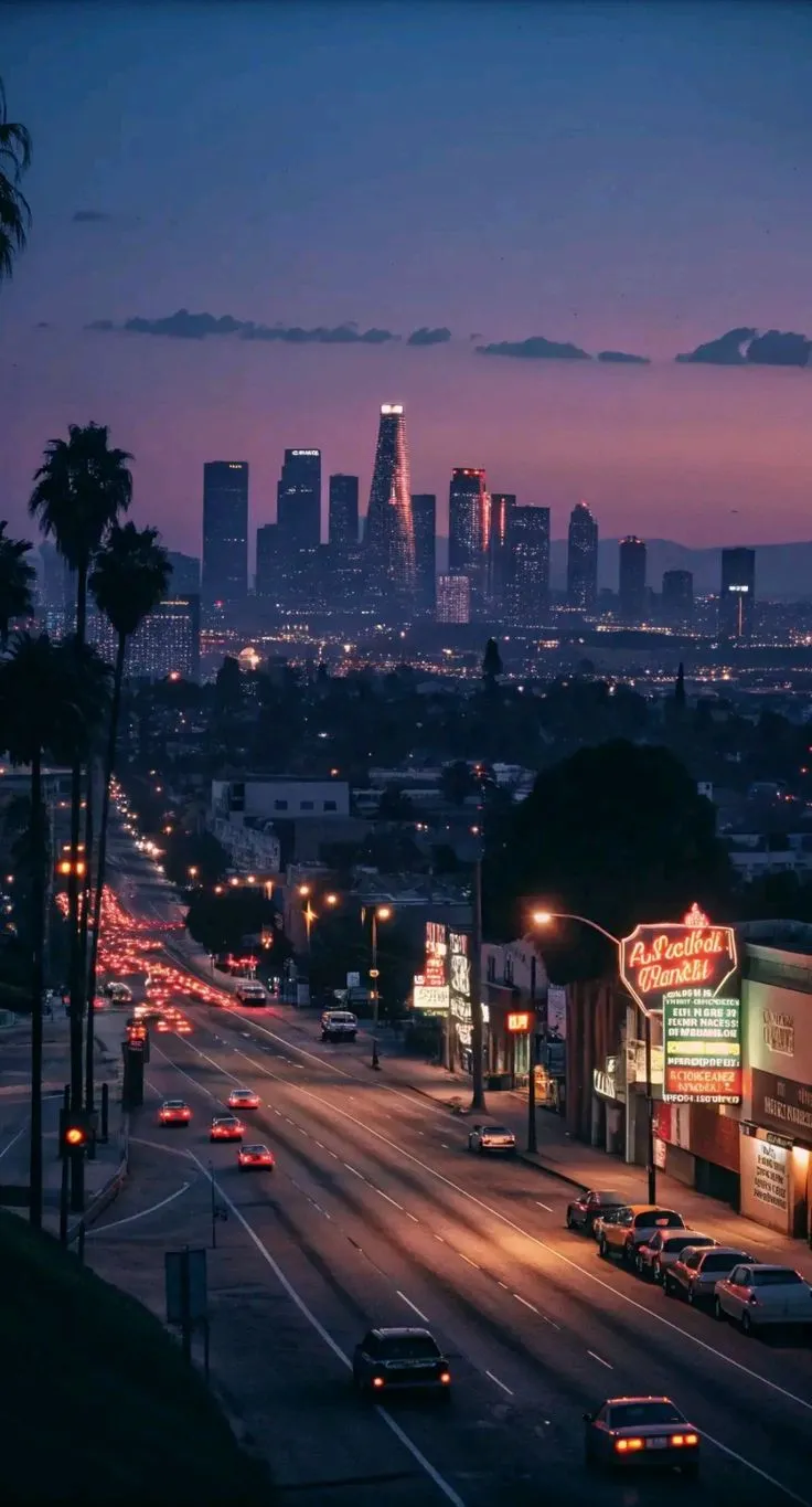 the city skyline is lit up at night with cars driving down the street in front of it